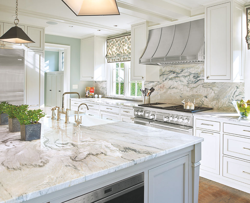 Bright white kitchen with dramatic quartzite countertops, matching stone backsplash, a large island, and custom range hood