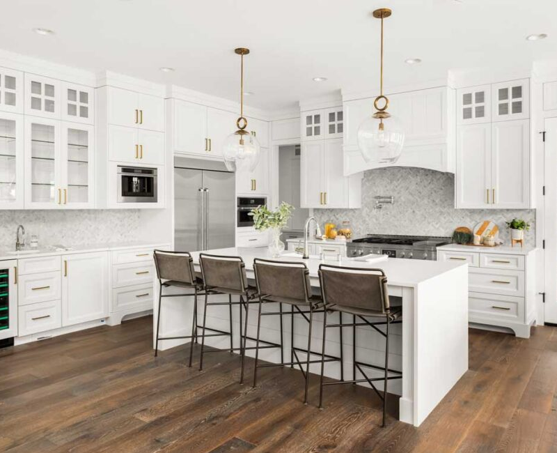 Bright white kitchen with Shaker cabinets, glass-front uppers, custom storage, and a large island with seating