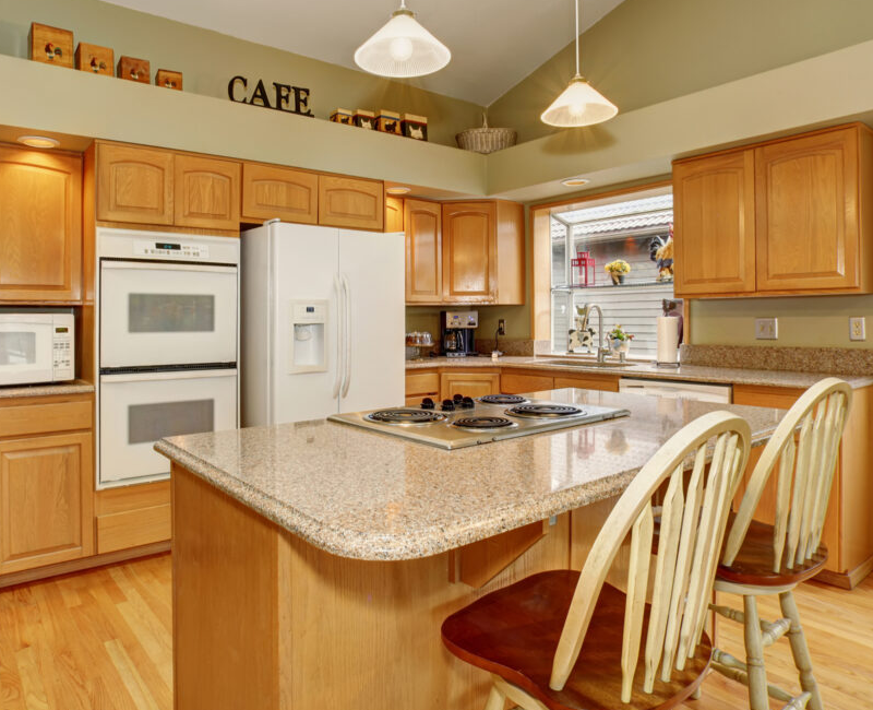 Dated kitchen with oak cabinets, white appliances, granite island cooktop, and limited modern storage features